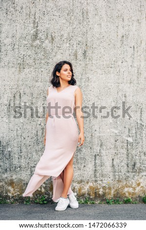 Urban fashion portrait of beautiful young woman posing on gray wall background