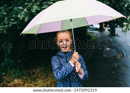 kid girl with umbrella, waterproof coat and boots jumping in puddle and mud in the rain. Kid walking in summer rain
