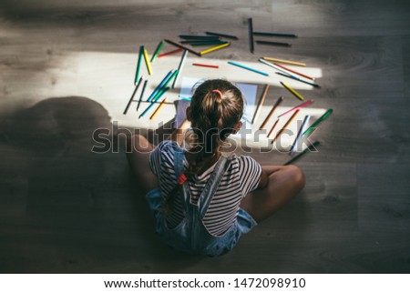 Kid girl drawing on floor on paper. Little girl writing on empty white paper. Blank paper and colorful pencils
