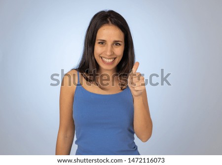 Portrait of beautiful young latin woman showing thumbs up sign feeling cheerful, happy and satisfied. Young happy student woman making thumb up in joyful approval gesture isolated on blue background.