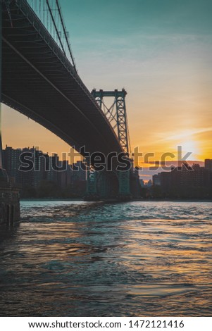 a beautiful shot from underneath the williamsburg bridge taken in brooklyn, new york, looking across the east river into manhattan during sunset. 
