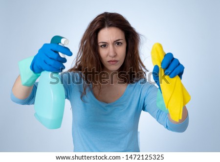 Angry and upset woman with cleaning spray and cloth cleaning feeling frustrated. The stain will not come out. In domestic duties and cleaning products advertising image isolated on blue background.