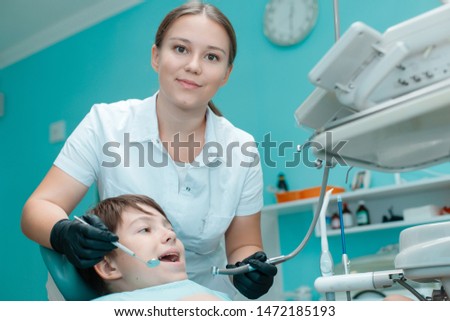 Patient in dental chair. Beautiful female dentist in black gloves work with a tooth drill and a mirror. Little boy having dental treatment at dentist's office.