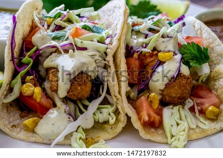 Oven fried Cod fish tacos, with cabbage tomatoes, roasted corn, avocado-cilantro sauce and salsa. Close up, head-on shot