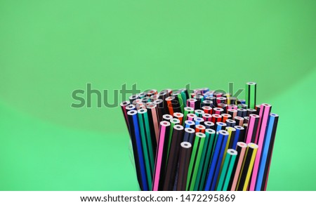 stand of many multi colored bright drawing pencils in a circular arrangement with a plain light green background. 