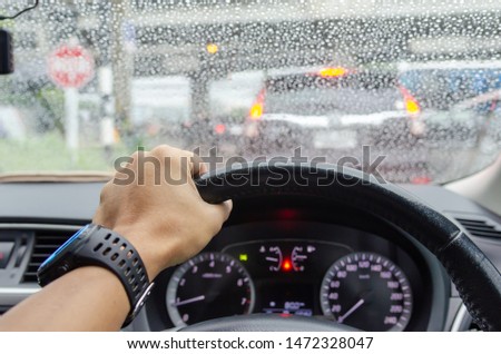 Hand driving rain blurred traffic jam background.