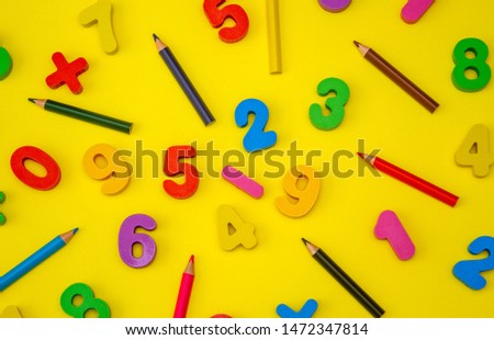 Bright colored, wooden numbers on a yellow background. Mathematical elements and symbols. View from above. Interesting school background for a postcard.