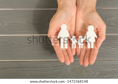 Woman holding figures of family in hands on grey wooden background, top view
