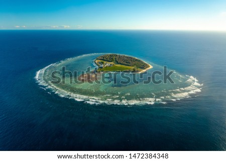 A small island surrounded by shallow coral reef in a deep blue ocean. Royalty-Free Stock Photo #1472384348