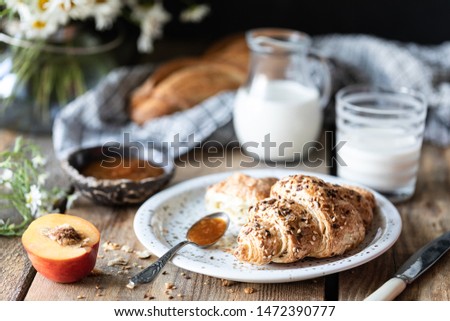Fresh bread and croissant with milk and peach or apricot jam on a wooden table. Bouquet of daisies. rustic.