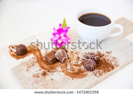 Coffee and milk chocolate with a pink flower, close up, delicious warm winter indulgence. Cocoa powder reminds one of cold winter night snacks. White cup close up marble board, lifestyle image
