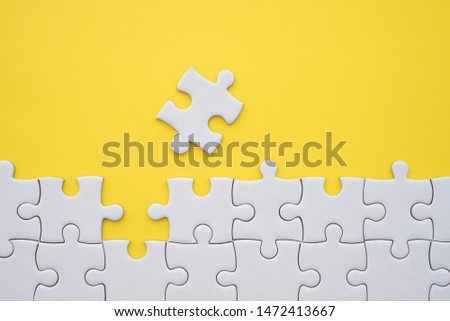 Unfinished white jigsaw puzzle on yellow background with copy space. Business strategy teamwork or problem solving concept. Teamwork is collaborative effort of team to achieve goal or to complete task