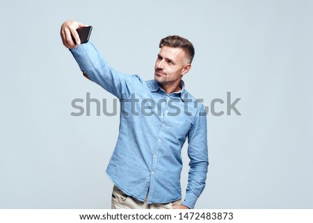 Catching happy moments Cheerful and handsome bearded man in casual wear making selfie while standing against grey background