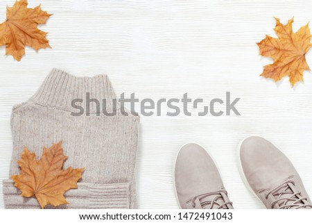 Autumn warm clothes. Trendy gray woolen sweater and comfort shoes on white wooden background with copy space. Female clothing. Fashion concept. Flat lay. Top View. 