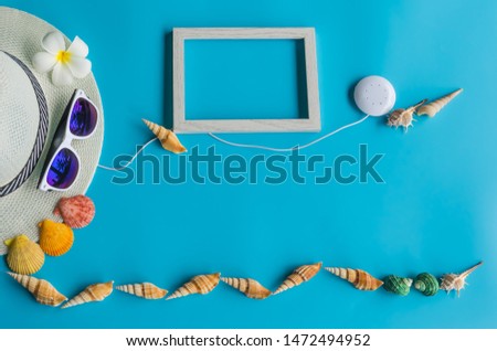 Summer    concept  setting  with  straw  hat,sunglasses,wooden  picture  frame,earphone  and  colorful  seashells  on  blue  background