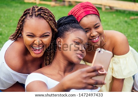 portrait of three beautiful african-american women afro braids dreadlocks and turban taking pictures of yourself on the phone in the park at a picnic,sisters on vacation