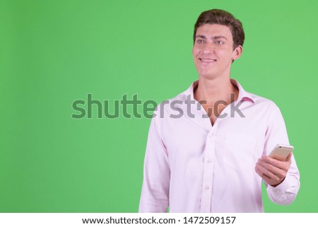 Portrait of young happy businessman thinking while using phone