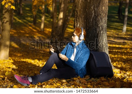 Relax time of Asian young man  lean the tree and looking Tablet as a listening to music in autumn season with a sunny light in the park