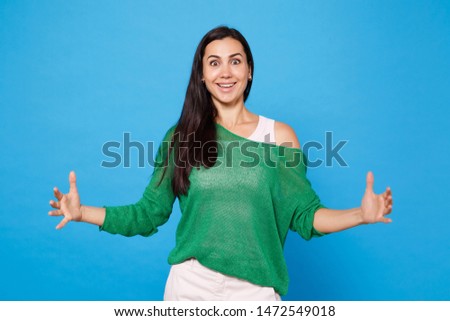 Portrait of excited cheerful young woman in green casual clothes gesturing demonstrating size with horizontal workspace isolated on blue wall background. People lifestyle concept. Mock up copy space
