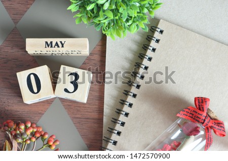 May 3. Date of May month. Number Cube with a flower, Rose bottle and notebook on Diamond wood table for the background.