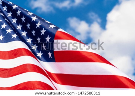 American flag on flagpole waving in the wind against white clouds