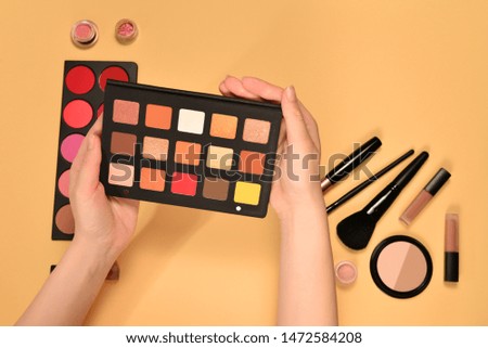 Eye shadow palette on woman hand. Professional makeup products with cosmetic beauty products, foundation, lipstick,  eye shadows, brushes and tools.