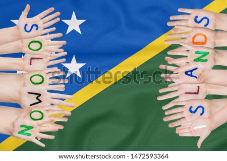 Inscription Solomon Islands on the children's hands against the background of a waving flag of the Solomon Islands