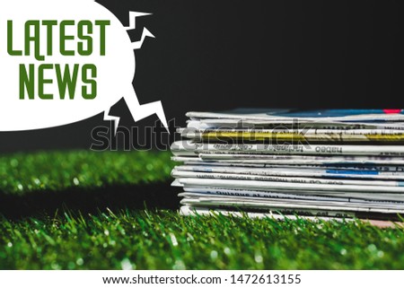 stack of different print newspapers on fresh green grass near speech bubble with green latest news lettering isolated on black