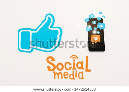 blue thumb up sign near smartphone with social media icons isolated on white