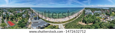Drone aerial perspective and panoramic view on sunny beach with sunbathers with windbreaks and towels at sea in touristic city.