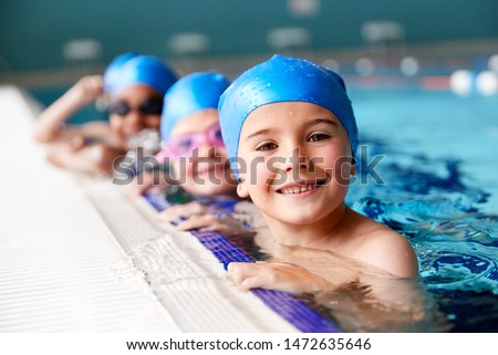 Portrait Of Children In Water At Edge Of Pool Waiting For Swimming Lesson