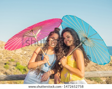 Young and smiling teenagers looking at camera and smiling with two colored umbrellas and the sea behind at sunset