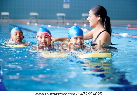 Female Coach In Water Giving Group Of Children Swimming Lesson In Indoor Pool Royalty-Free Stock Photo #1472654825