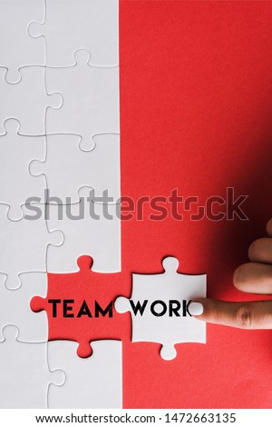 top view of woman pointing with finger at jigsaw near connected puzzle pieces with teamwork lettering on red