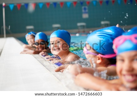 Portrait Of Children In Water At Edge Of Pool Waiting For Swimming Lesson