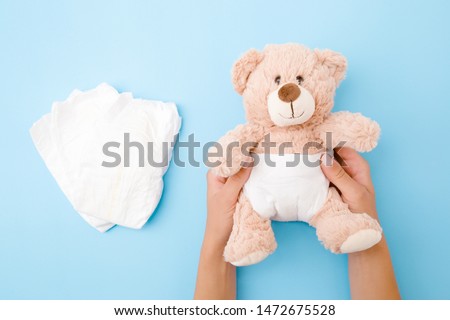 Woman hands holding brown teddy bear with white diaper on pastel blue background. Closeup.