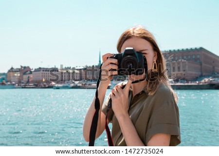Travel trip concept. Cute blonde girl with a camera in her hands takes pictures of the city, traveling on vacation in the summer.
