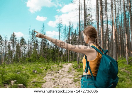 Lovely girl with a backpack shakes his hand to the side, walking in the forest, enjoys the beautiful hills on a sunny day.