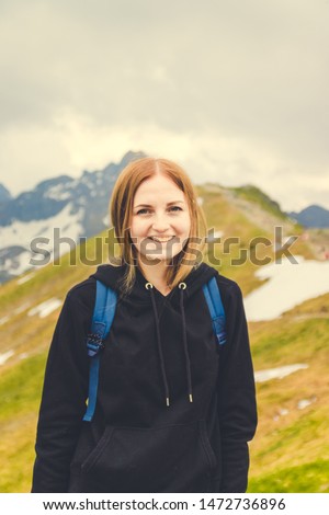 Cute blonde girl in a warm gray sweater climbed the peak of the mountain and looks at the photographer s camera. Travel day concept. Tourist adventures