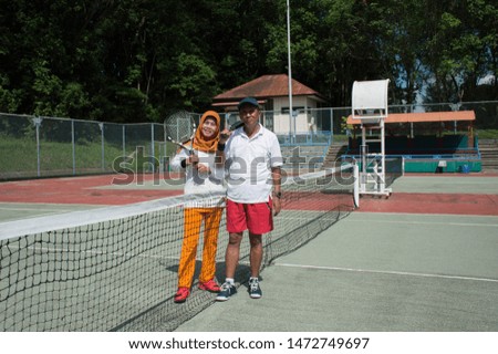 Portrait of an active asian muslim senior couple standing at outdoors tennis hard court and ready to play tennis. at sunny days