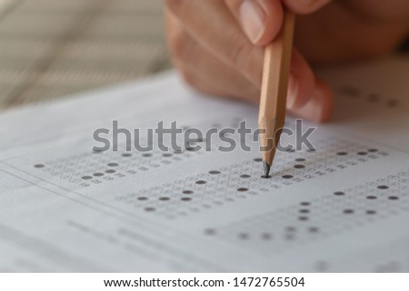 Student hand testing doing test exam with pencil drawing selected choices on answer sheet in school final exams at college or university. Taking multiple choice for assessment in examination classroom