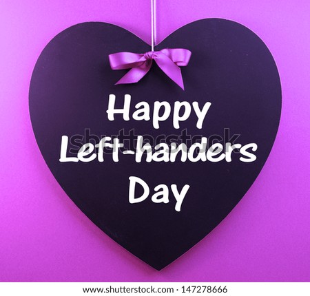Happy Left-handers Day message sign text written on heart shape blackboard hanging against a purple background for International Left-handers Day celebrated on August 13. Royalty-Free Stock Photo #147278666