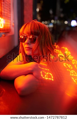 Portrait of ginger woman with sunglasses and yellow t shirt on red neon lights            