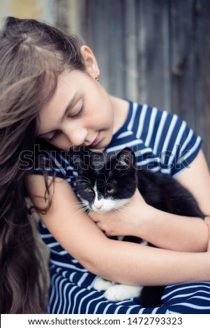 Black kitten in the arms of a girl with long hair and in a striped dress.