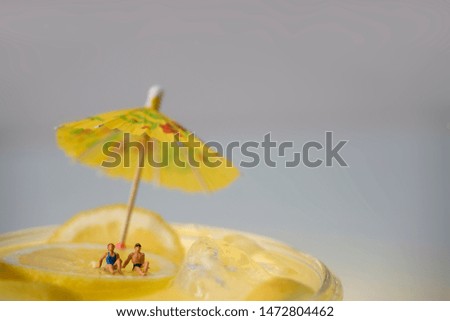 Miniature people in swimsuits relaxing in a lemonade soda. Use as a concept of: Holidays, relaxation, enjoying a lemonade, travel