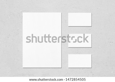 One empty white vertical a4 sized poster and three horizontal rectangle business card mockups with soft shadows on neutral light grey concrete wall background. Flat lay, top view
