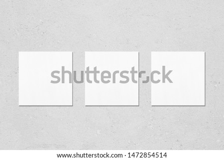 Three empty white square business card mockups with soft shadows on neutral light grey concrete wall background. Flat lay, top view