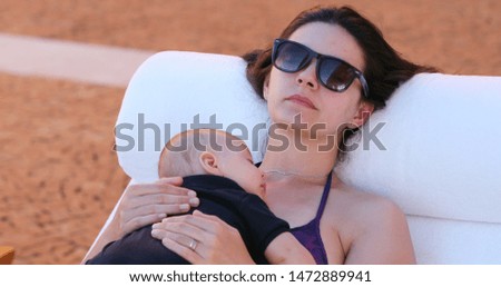 Mother and baby infant taking a nap together by the swimming pool outside.