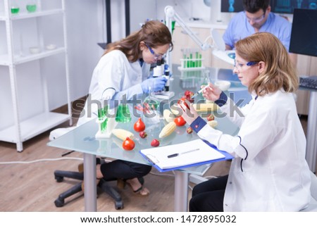 Team of scientist working together in a research lab doing biological test on tomatoes. Test tubes with green solution.