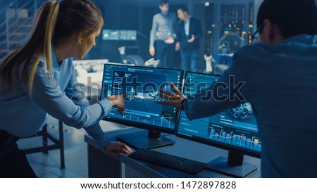 Female and Male Engineers are Discussing the 3D CAD Software Render of an Electric Concet Car. High Tech Laboratory with a Prototype Vehicle Chassis. Royalty-Free Stock Photo #1472897828
